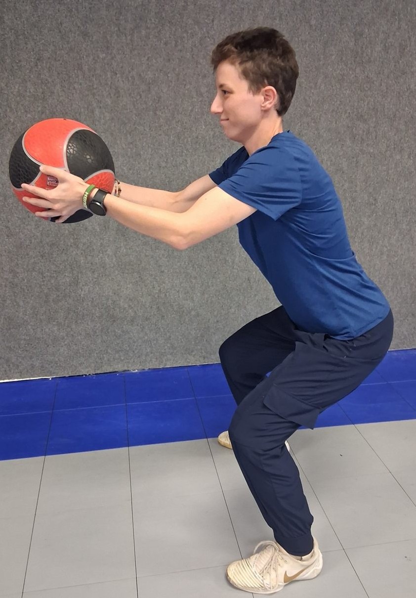 Dion smiling while holding a medicine ball out in a squat